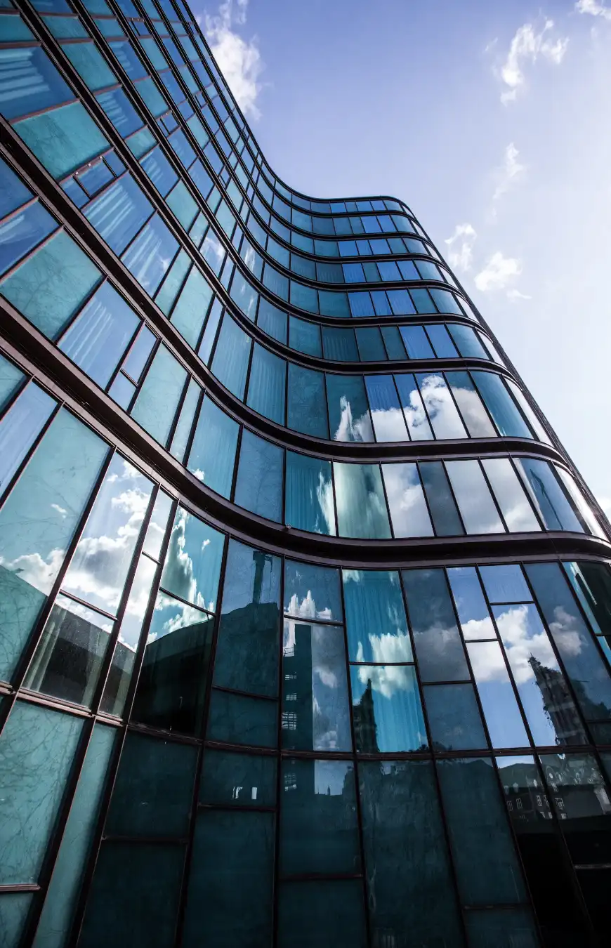 Moderna fachada de vidrio curvado reflejando el cielo, destacando la innovación en diseño arquitectónico de vidrio.