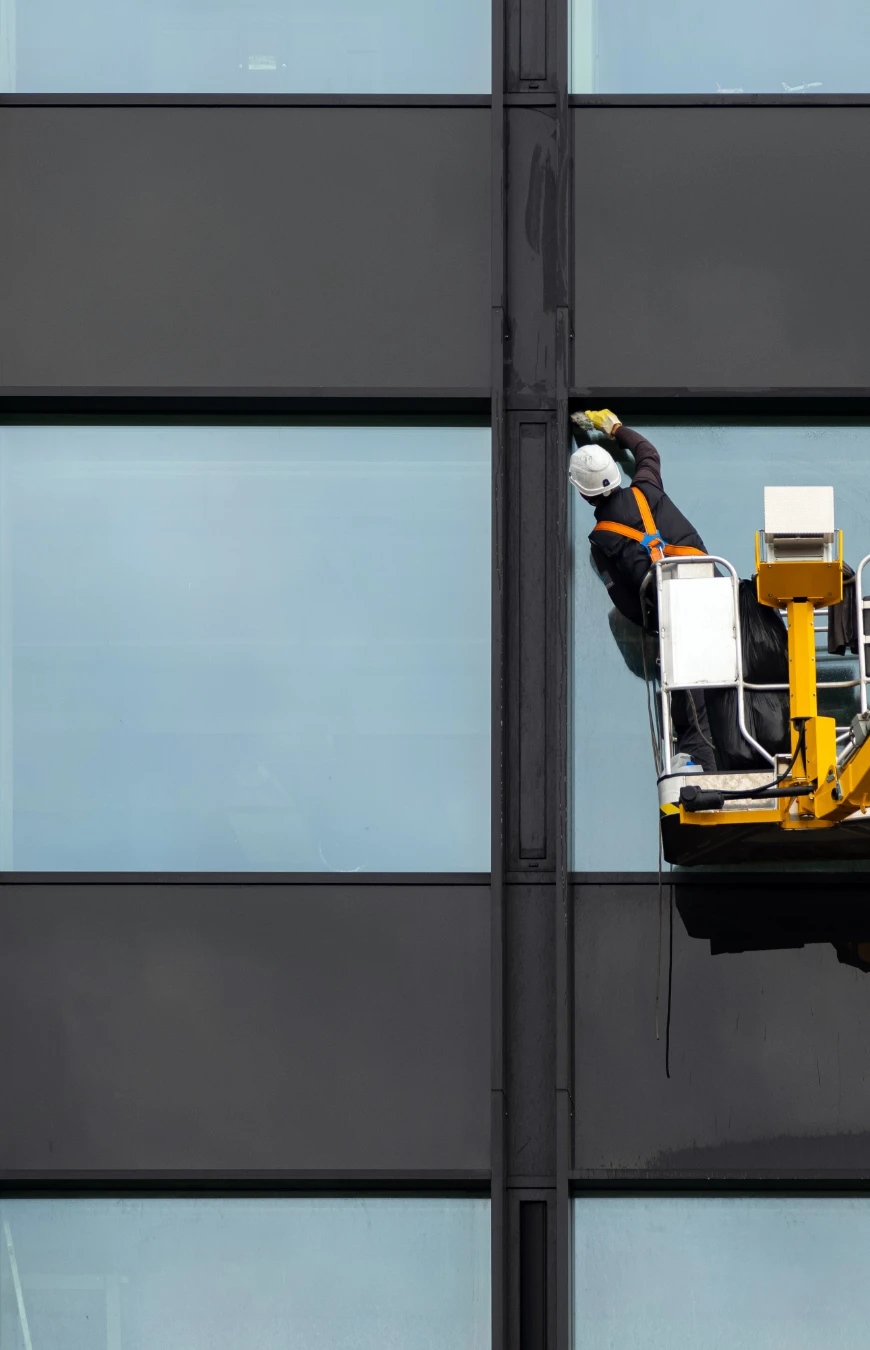 Trabajador instalando vidrio en un edificio, enfatizando el servicio profesional de instalación ofrecido por Romano Glass.